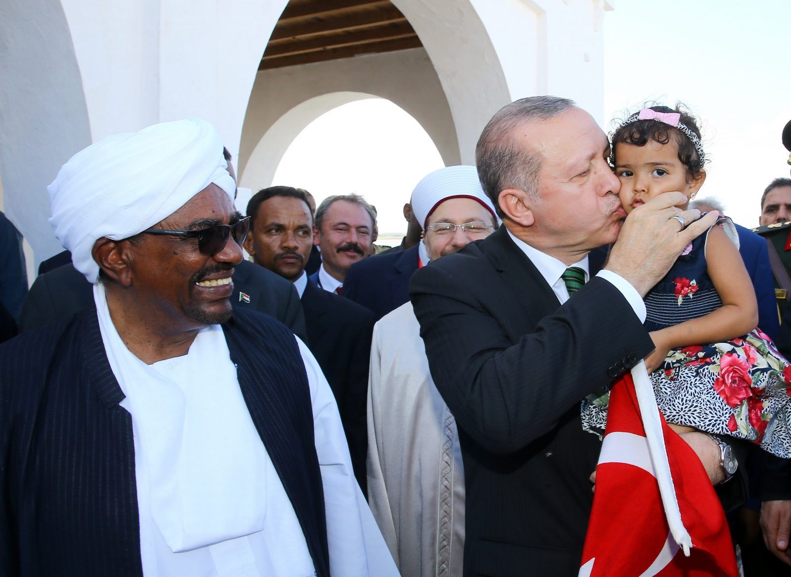 الرئيس التركي رجب طيب إردوغان يقبل طفلة صغيرة وهو يسير مع الرئيس السوداني عمر البشير خلال زيارته في بورتسودان – 25 ديسمبر 2017. وقام إردوغان بجولة في جزيرة سواكن في اليوم الثاني من زيارته. (أ.ف)